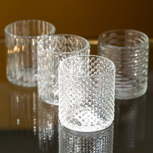 Four patterned glass tea light holders with textured designs on a reflective surface.