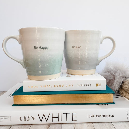 be kind and be happy set of large ceramic mugs shown on stack of books