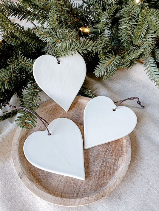 set of three large hanging white ceramic hearts on wooden tray with Christmas foliage