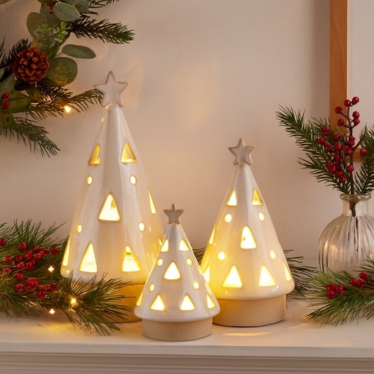 Decorative LED lit ceramic Christmas trees on a mantel piece with festive decorations.