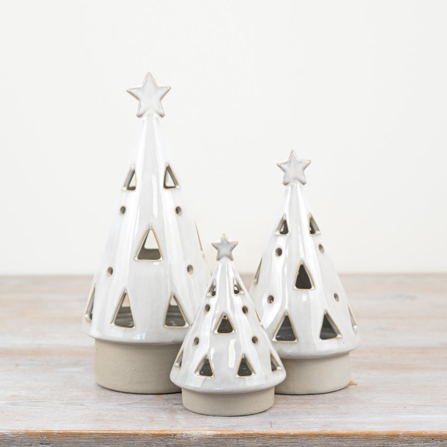 Three white ceramic Christmas tree-shaped LED lanterns with star decorations on a wooden surface.