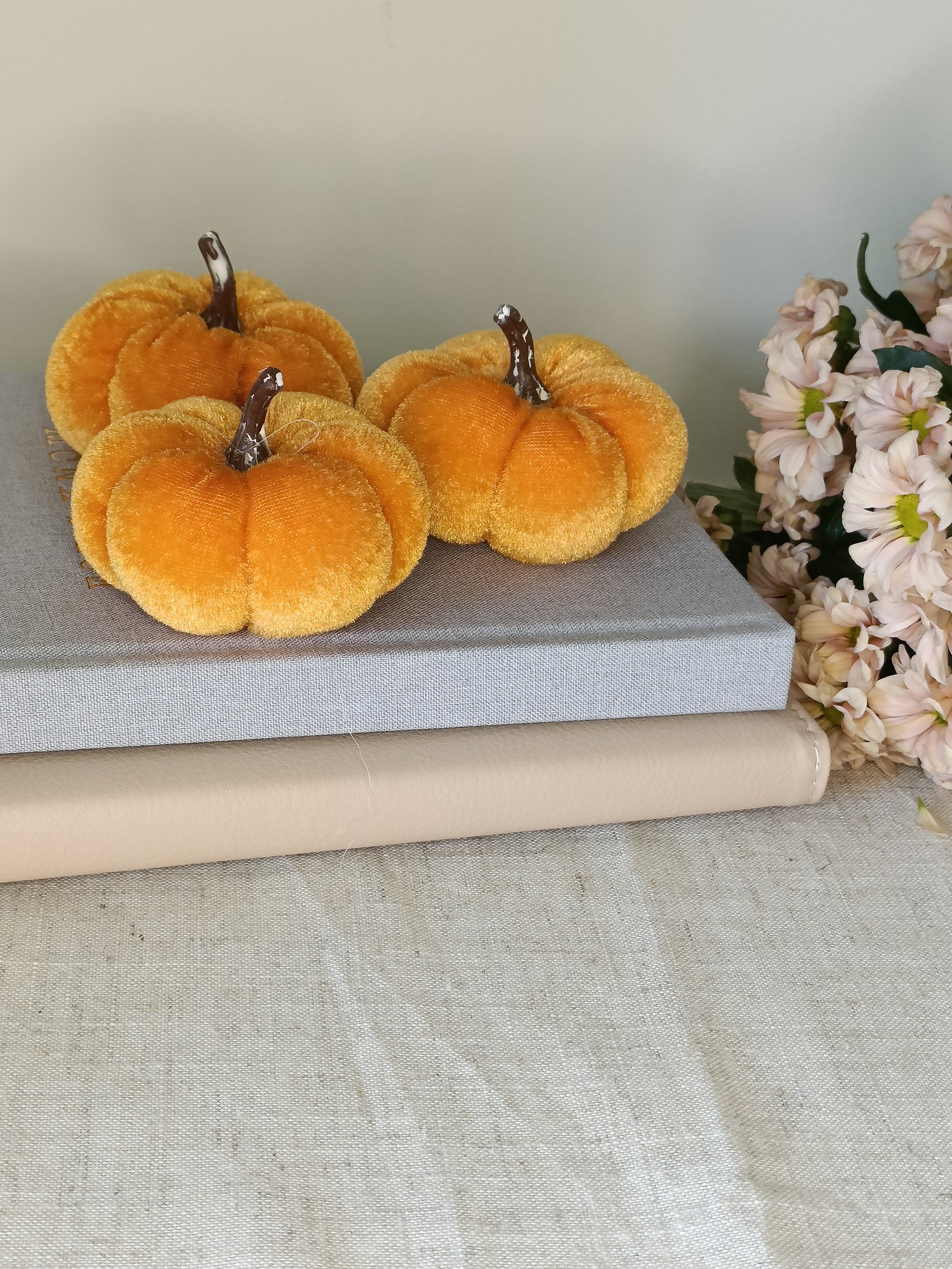 Three orange pumpkins on a gray surface with a bouquet of flowers in the background.