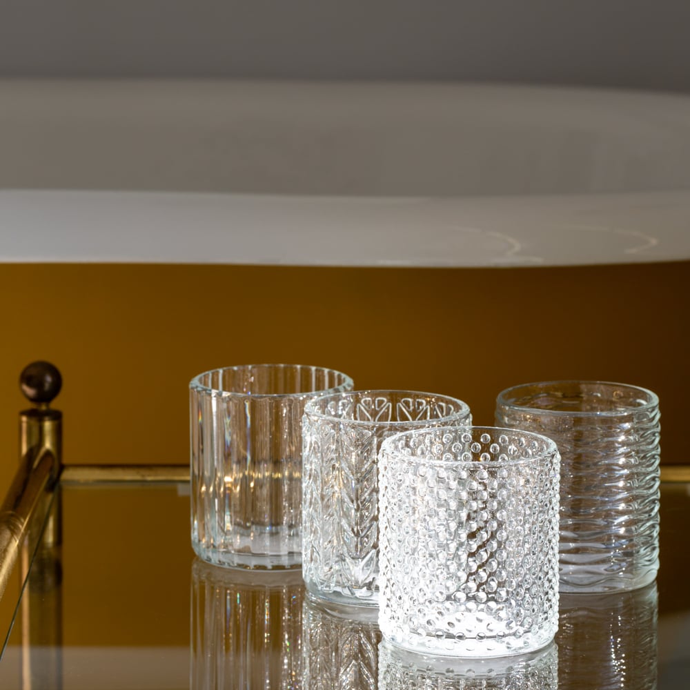 Four patterned glass tea light holders with textured designs on a reflective surface.